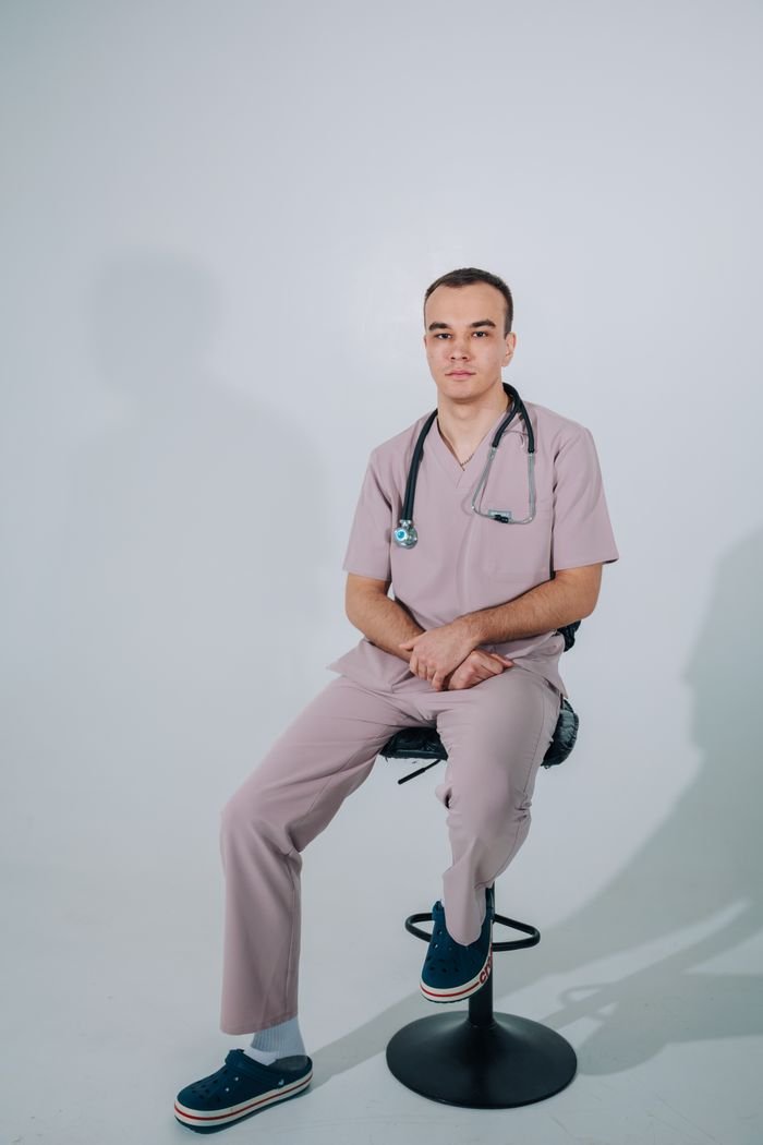Portrait of a male nurse sitting with stethoscope in a well-lit studio.