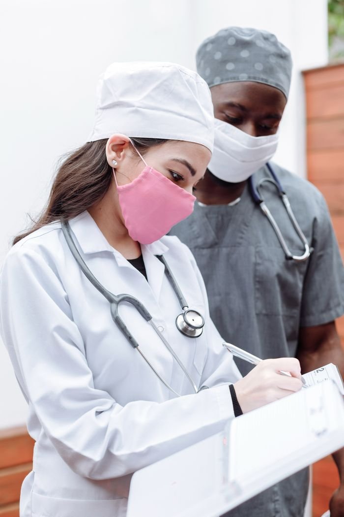 Doctors in scrubs and masks discussing a medical chart indoors, exemplifying teamwork in healthcare.