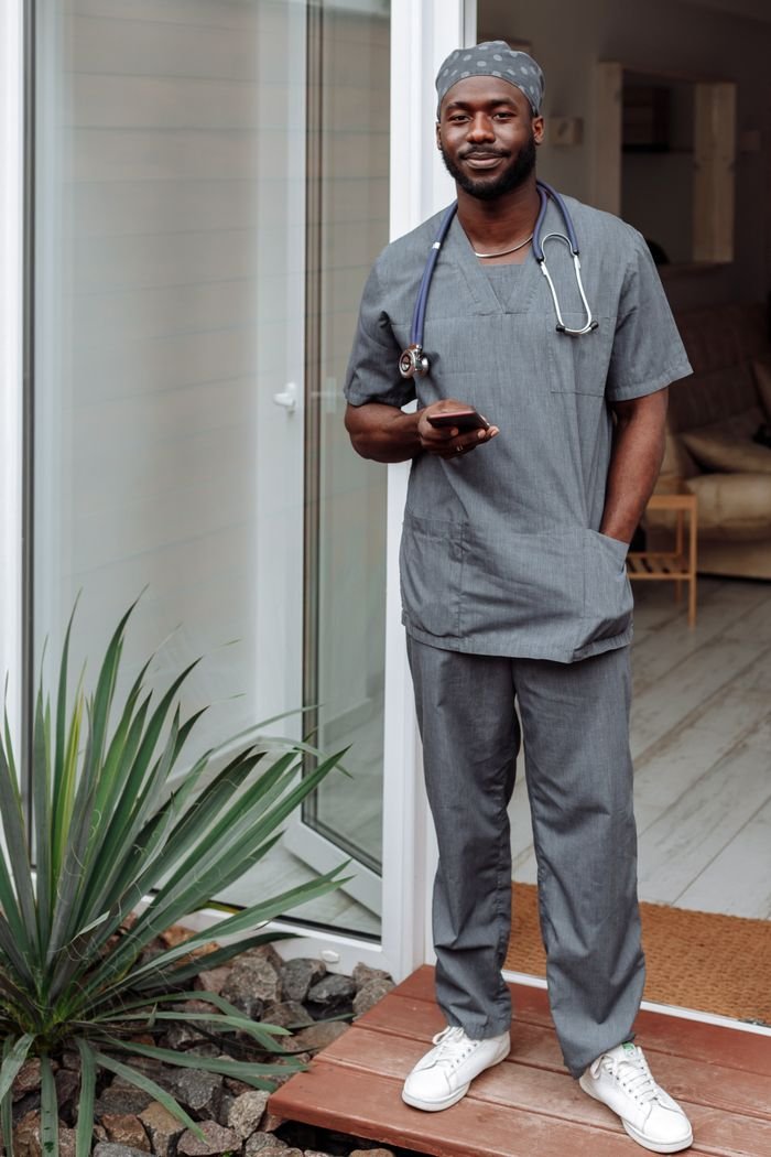 A healthcare professional in gray scrubs, holding a phone indoors.