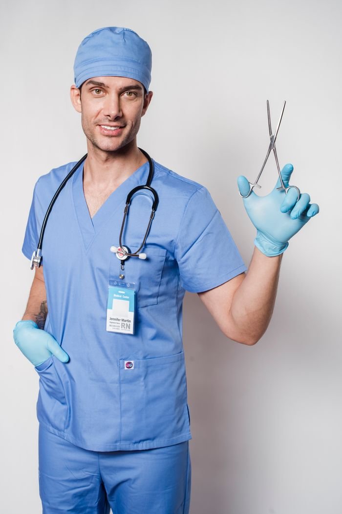 Professional specialist in blue medical clothes and latex gloves looking at camera and showing forceps